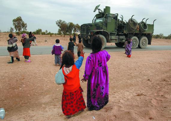 Military vehicle greeted by a group of children in Afghanistan.