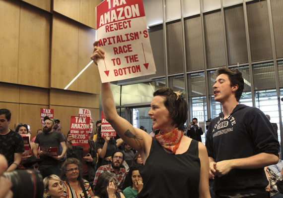 BBVA-OpenMind-ilustración-gonzalez-nueva-ilustracion-digital_papel-industria-financiera_At a municipal vote in Seattle, various demonstrators hold signs demanding that locally based multinational corporations, such as Amazon, be taxed to combat rising housing prices